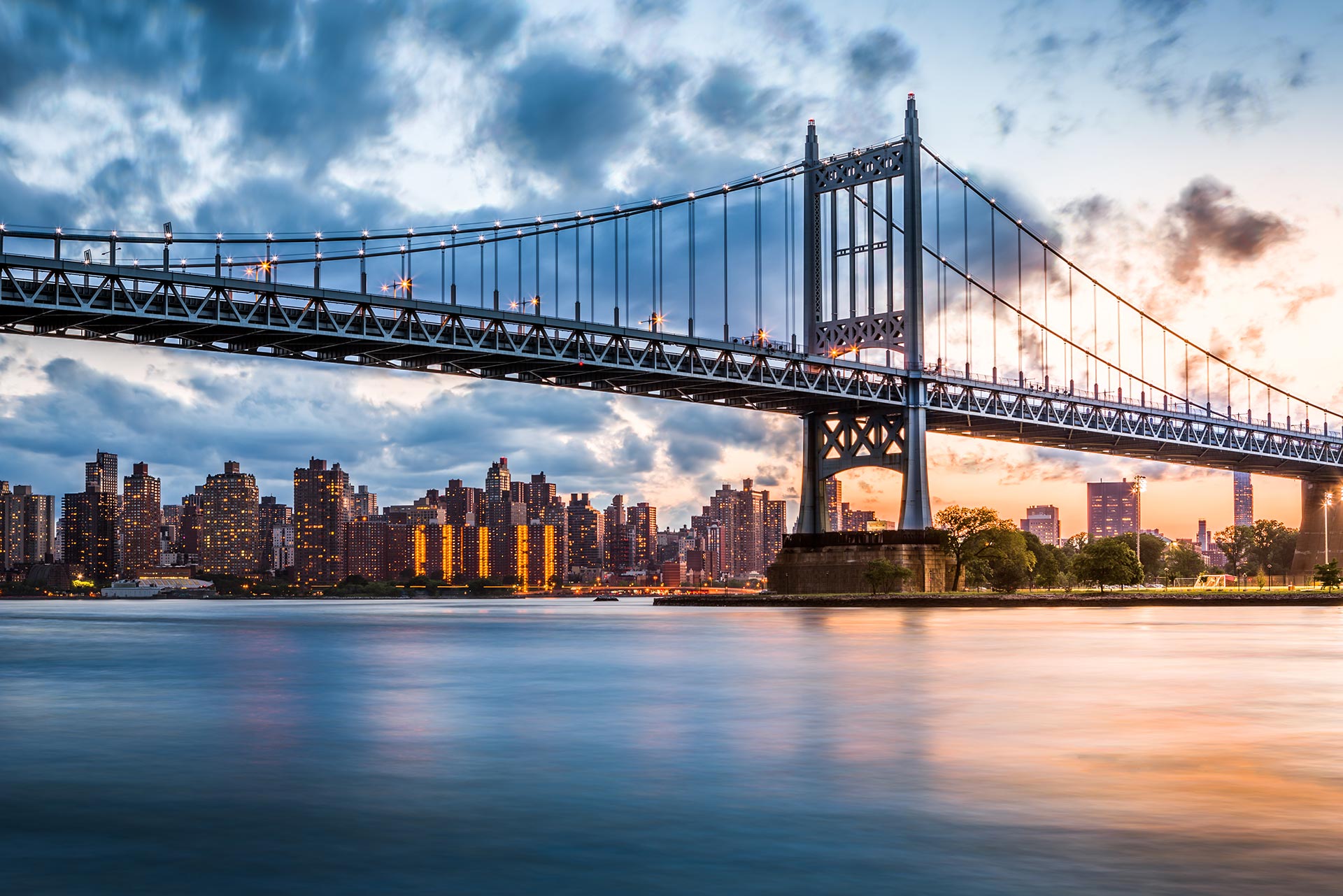 A suspension bridge spans over a river at sunset with a city skyline in the background, where business & litigation lawyers work as clouds drift across the sky.