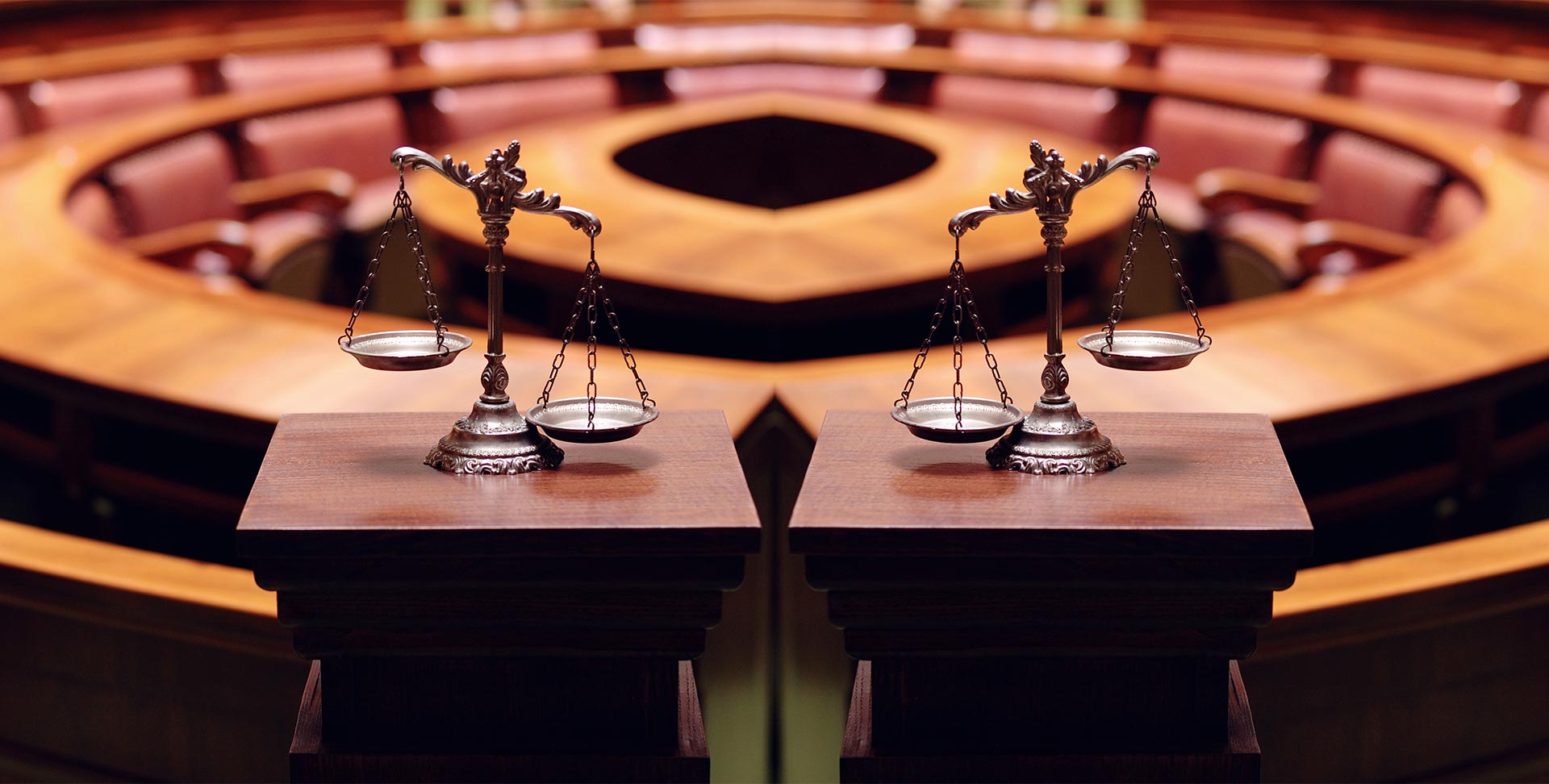 Two scales of justice placed on wooden podiums in an empty courtroom with curved rows of seats in the background, reflecting the environment where a commercial litigation attorney NYC might advocate for clients.
