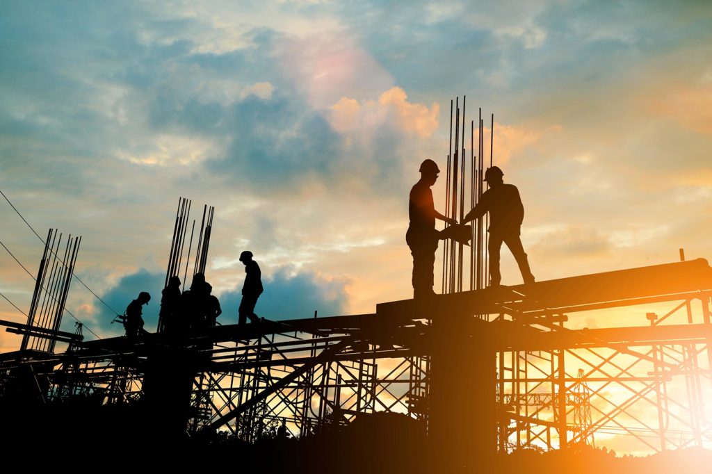 Silhouetted construction workers stand and work on scaffolding at a building site during sunset, with steel rods visible against the sky—a scene familiar to any construction litigation lawyer NYC.