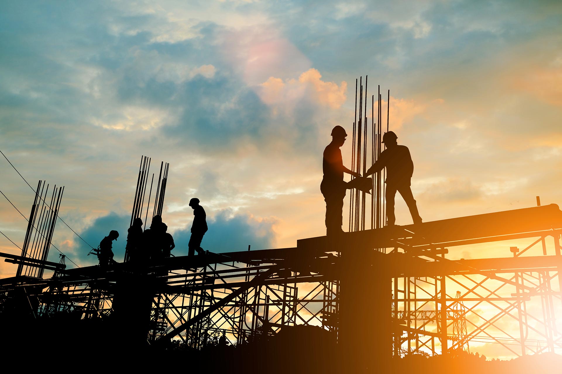 Silhouetted construction workers stand and work on scaffolding at a building site during sunset, with steel rods visible against the sky—a scene familiar to any construction litigation lawyer NYC.