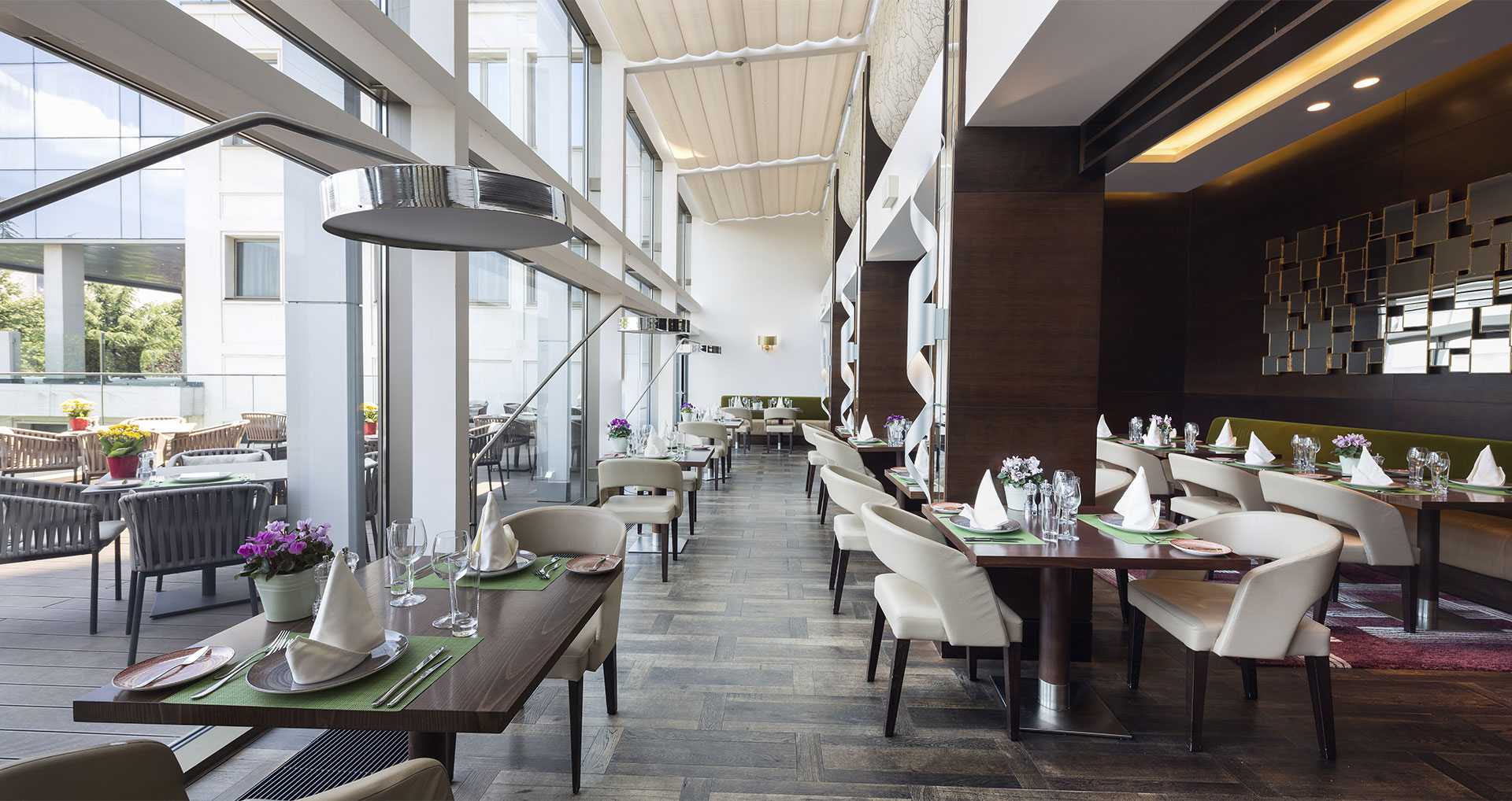 Modern restaurant interior with neatly set tables, white chairs, wood floors, large windows, and outdoor seating visible through glass doors—an ideal spot for business & litigation lawyers to meet clients in a stylish setting.