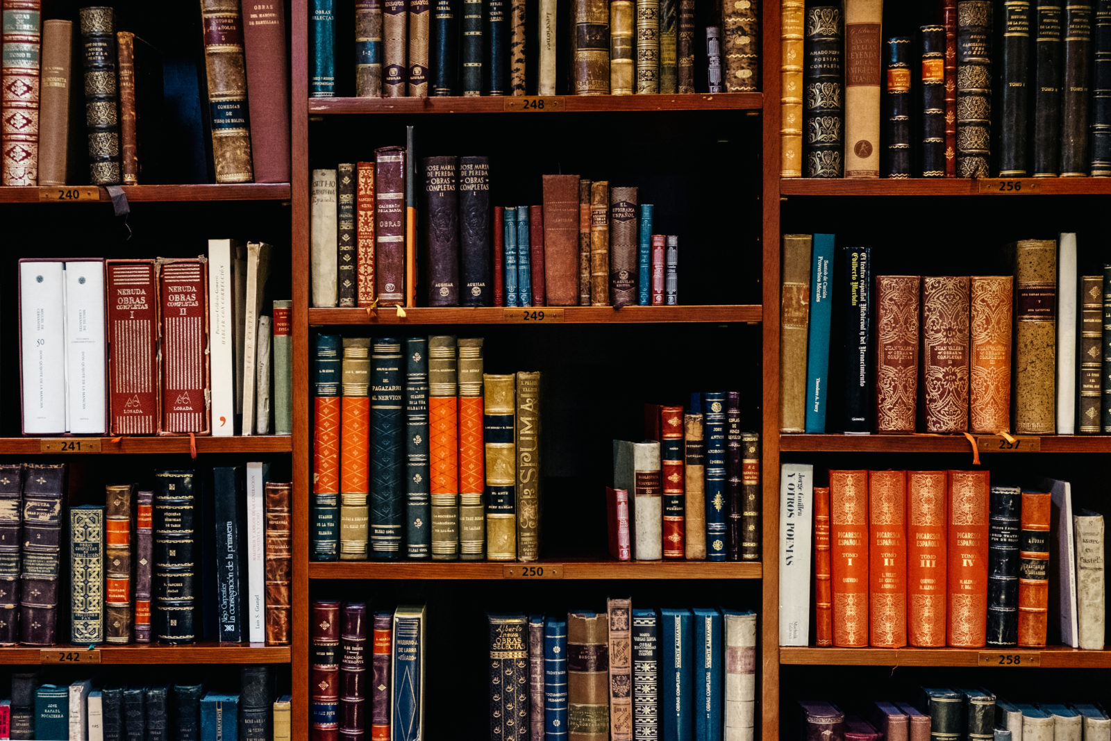 A wooden bookshelf filled with various old and colorful books, arranged vertically and horizontally on multiple shelves.