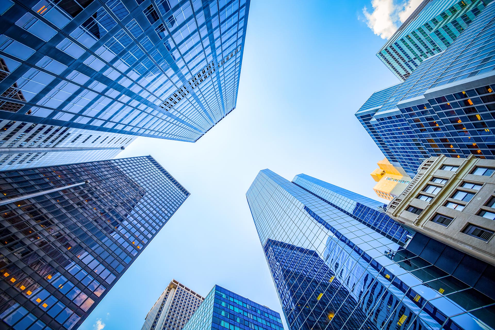 Looking up at tall modern skyscrapers with glass and steel facades against a blue sky in a city bustling with business startup law firms.