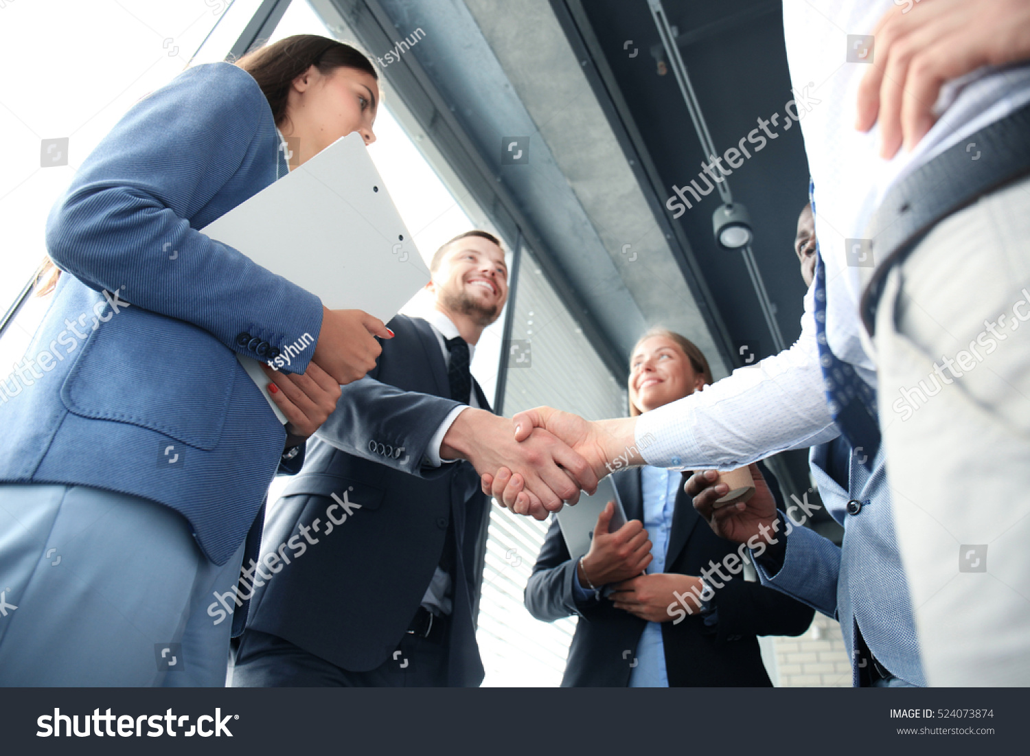 Group of business professionals in suits shaking hands and smiling during a meeting in a modern office setting. For collaboration opportunities, contact us.