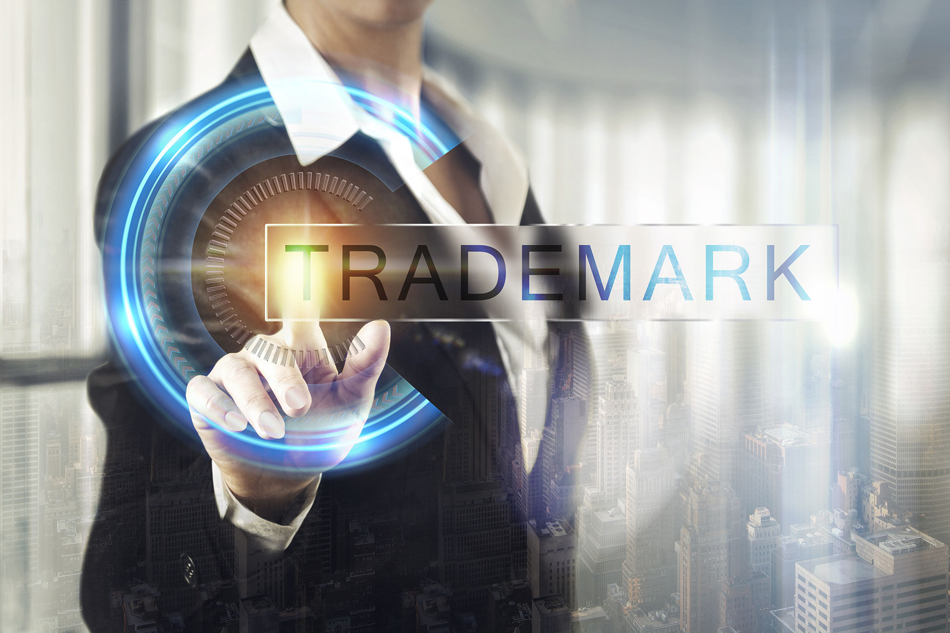 A person in business attire touches a virtual interface displaying the word "TRADEMARK," highlighting trademarks amid digital graphics and a cityscape in the background.