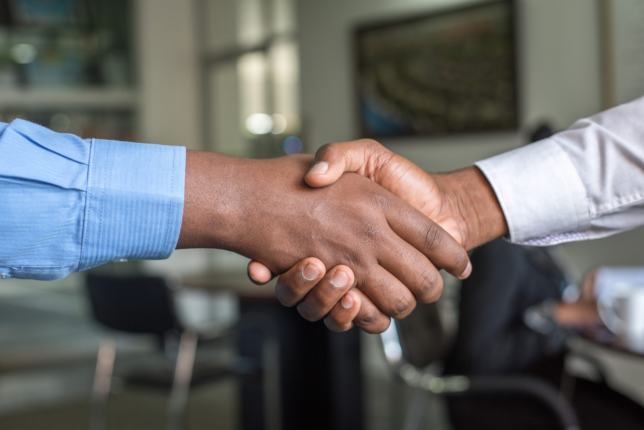 Two people wearing dress shirts shaking hands in an office setting.