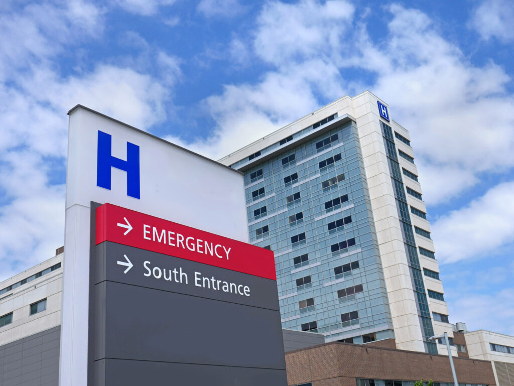 A hospital building with a sign directing to the emergency room and south entrance under a partly cloudy sky, resembling locations often visited by a NYC personal injury lawyer after an accident.