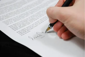 A hand holding a fountain pen signs a document with printed text.